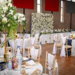 Basketball court transformed into a wedding reception with white, gold, and navy décor, floral centrepieces, and draped chairs