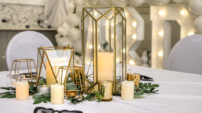 Varied heights of gold hexagonal candle holders with greenery and LED candles as elegant event décor