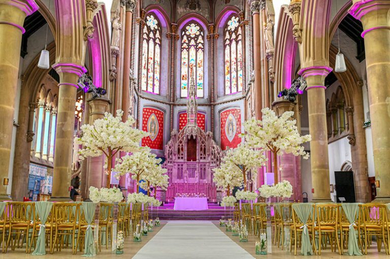 Wedding ceremony set up at Gorton Monastery with blossom trees and cylinder vases with floating candles lining the aisle