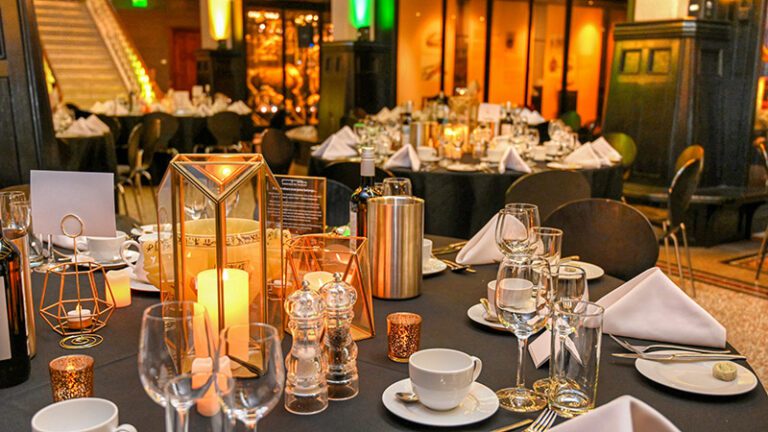 Gold themed centrepiece with hexagonal vases, LED candles, and small candle holders set among historical artefacts at Manchester Museum corporate dinner