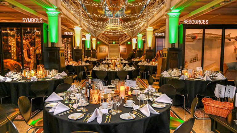 Complete view of Manchester Museum event room with black tablecloths, gold-themed centrepieces, and historical artefacts