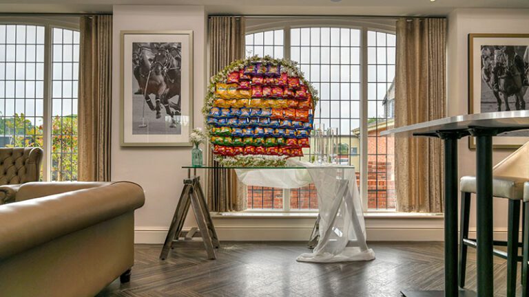 Mesh wall with 60 assorted crisps, floral garland, vases with floral stems, and glass sleeve candle holders at Colshaw Hall, Cheshire