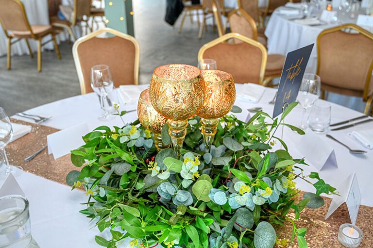 A set of 3 golden goblets placed in the middle of green foliage wreath