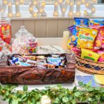 A candy cart displaying a basket of assorted crisps, a lot of mini chocolates and plastic jars filled with sweets