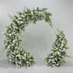 Luxury broken arch floral moongate with full green foliage and white roses, designed as an elegant backdrop for weddings and events.