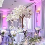 Wedding reception room decorated with white blossom tree centrepieces and soft up lighting at Hollins House, Macclesfield